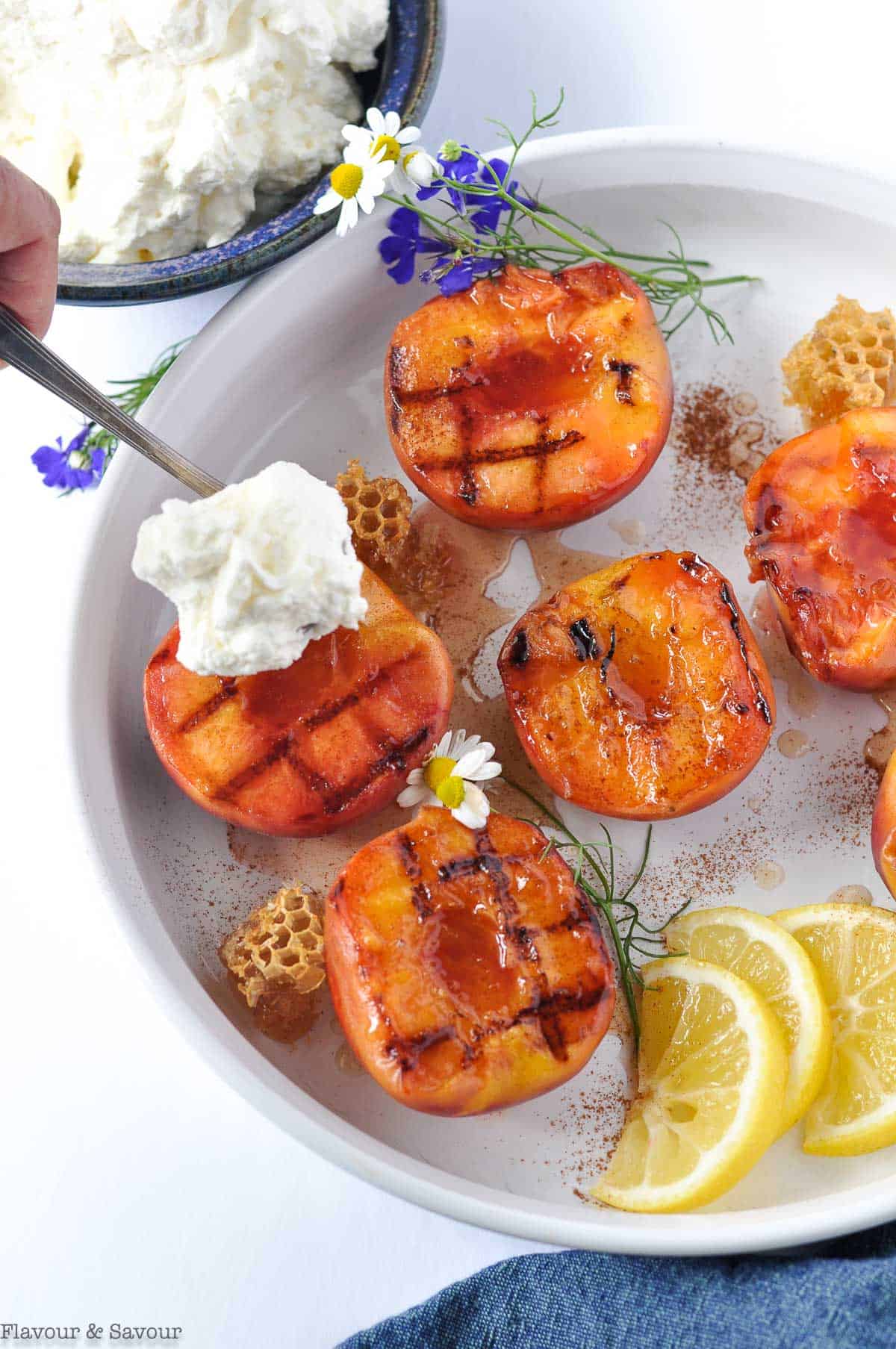 Spooning whipped cream on to a grilled peach half.