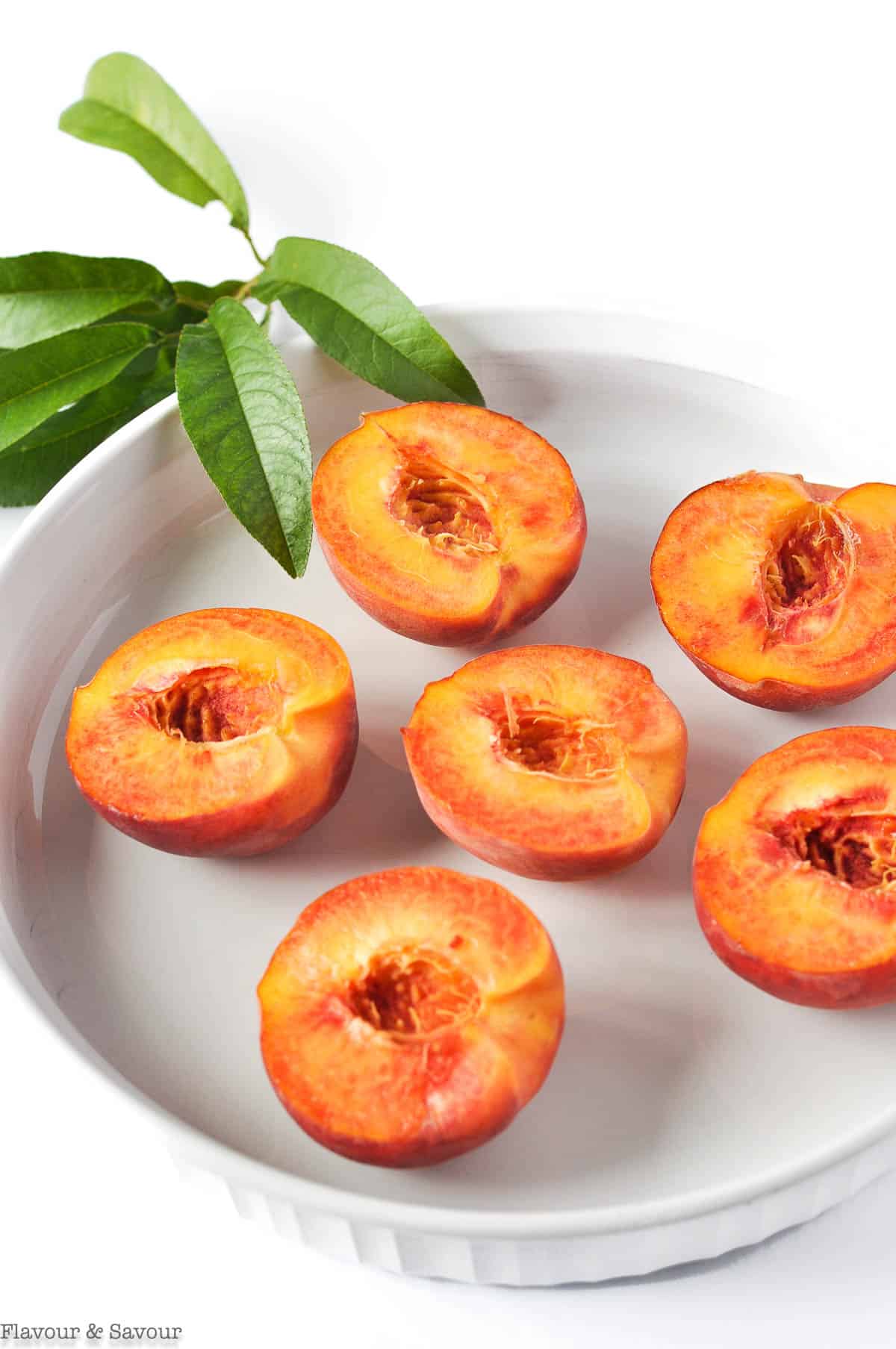 Peach halves in a white shallow dish with peach leaves.