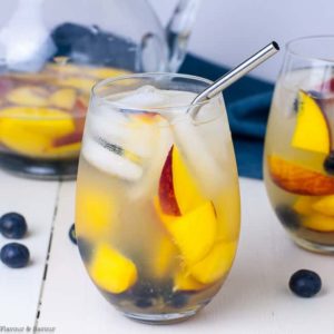 A glass of The Best Peach Sangria with fresh peaches and blueberries.