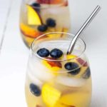 Two glasses of Peach Sangria with peaches and blueberries.