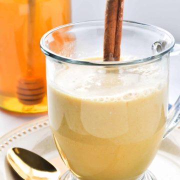 Warm Turmeric Cinnamon Milk in a clear mug with a cinnamon stick