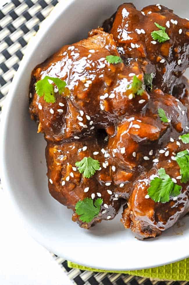 Super-easy Crock Pot Sticky Chicken thighs in an oval serving dish garnished with cilantro and sesame seeds.