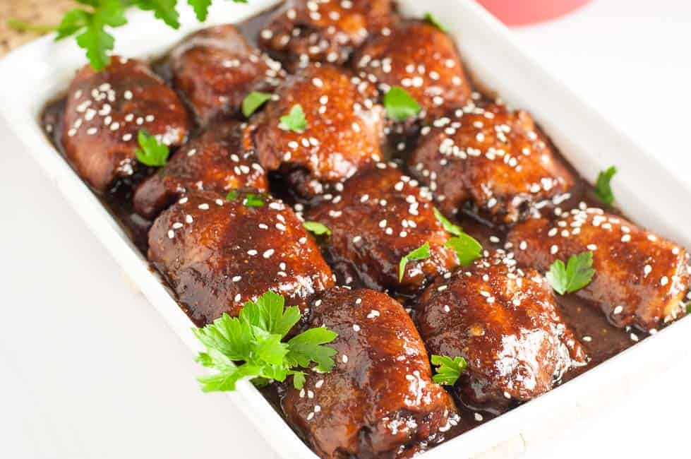 Slow Cooker Sticky Chicken thighs in a white serving dish garnished with cilantro and sesame seeds.