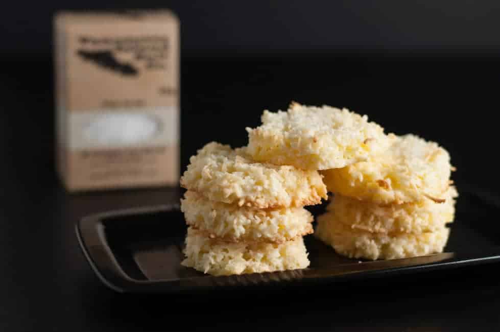 Crispy Salted Coconut Cookies with sea salt. Cookies stacked on a tray with a box of Vancouver Island Sea Salt in the background.