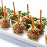 Mini Cheese Balls skewered with a pretzel stick. on a white platter.