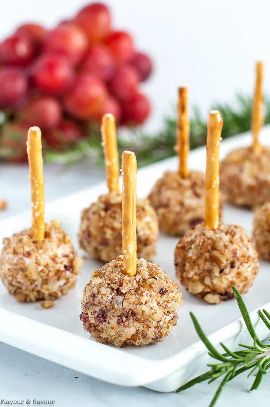 Close up view of mini cheese balls with pretzel sticks on a white dish with rosemary sprigs