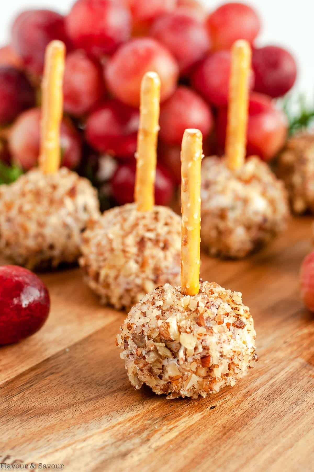 close up view of Mini Cheese balls with pretzel sticks on a board with grapes