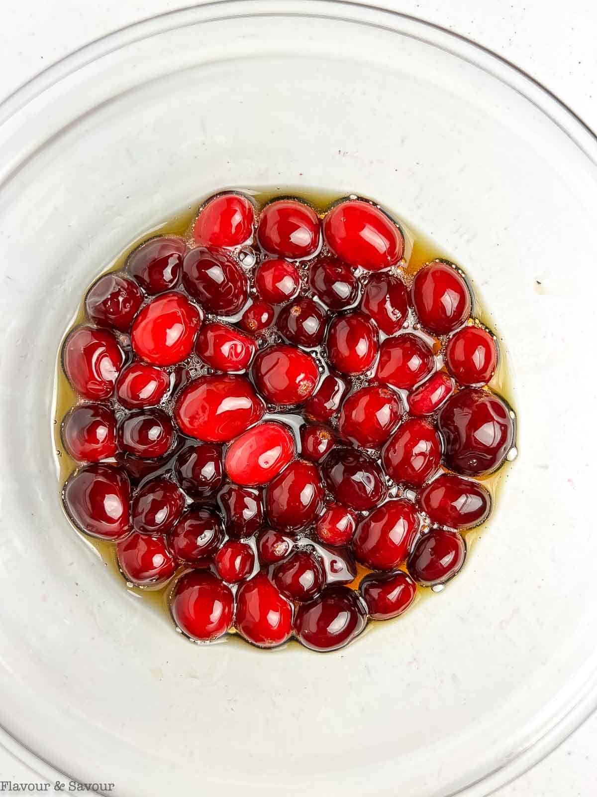 Sugared cranberries soaking in maple syrup in a glass bowl.