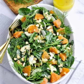 A shallow bowl of kale salad with Cara Cara oranges and toasted almonds