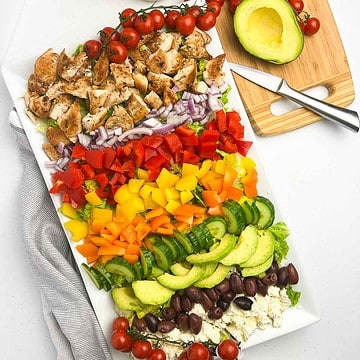 Greek chicken Cobb Salad ingredients in rows on a large white platter.