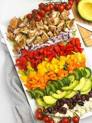 Greek chicken Cobb Salad ingredients in rows on a large white platter.