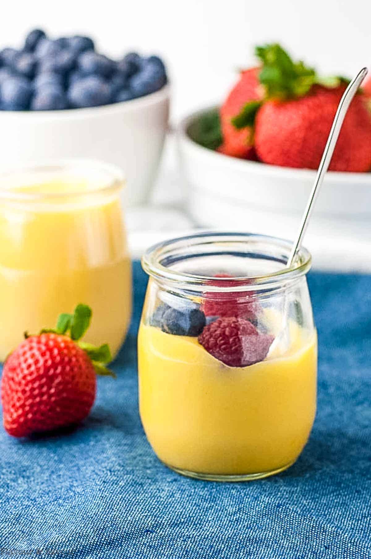 A tiny jar of lemon curd with blueberries and strawberries in the background.