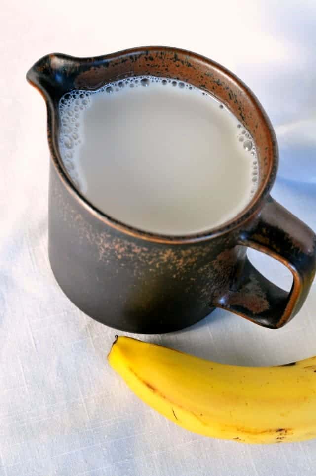 A brown stoneware jug of milk with a banana beside it.