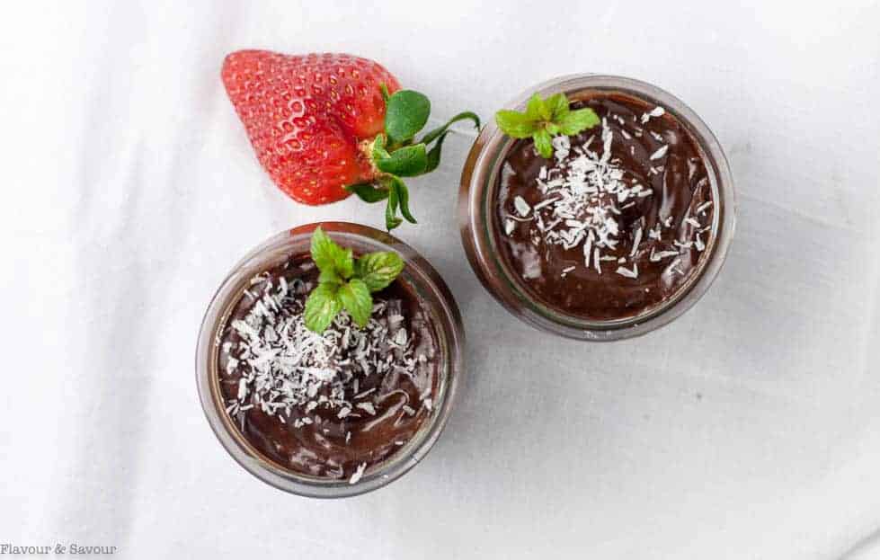 Chocolate Mousse in two small dessert jars garnished with coconut and a fresh strawberry