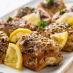 Easy Baked Lemon Chicken on a serving platter with fresh herbs and lemon