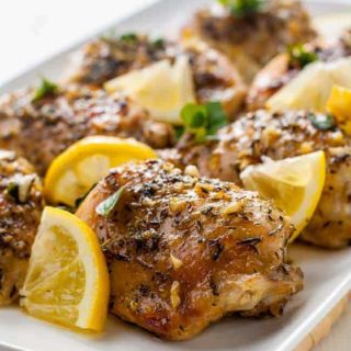 Easy Baked Lemon Chicken on a serving platter with fresh herbs and lemon