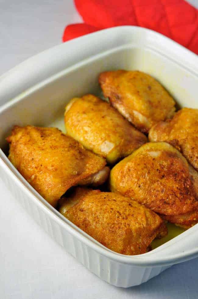 6 seared chicken thighs in a square white baking dish