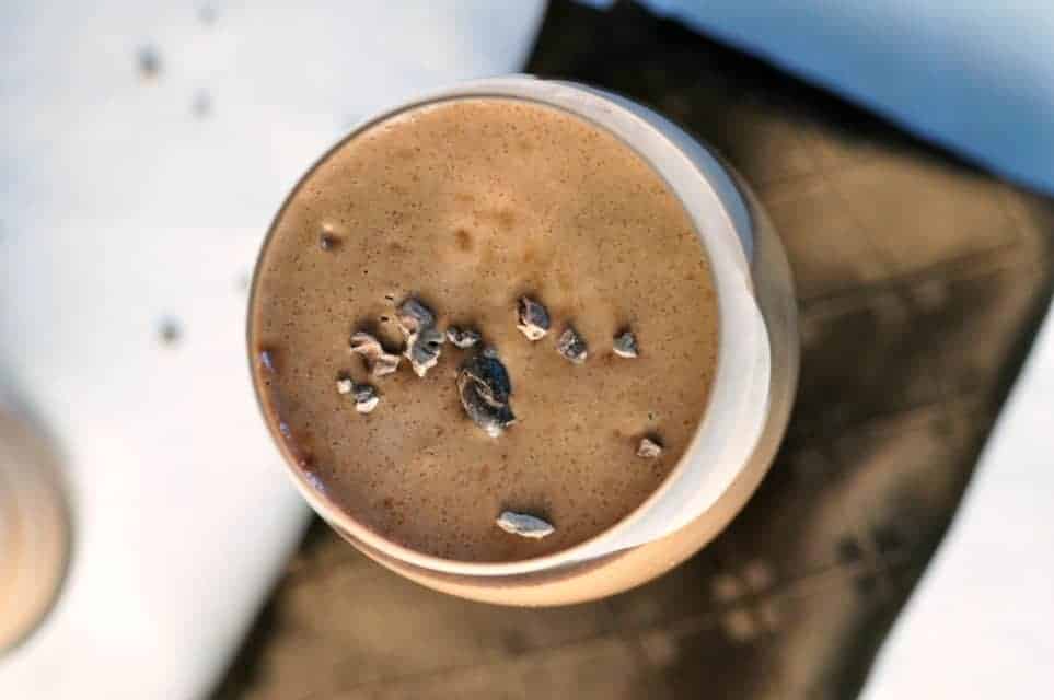 Overhead view of a glass of chocolate almond smoothie with cacao nibs.