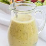 a small pitcher of Everyday Honey Citrus Vinaigrette with salad in the background