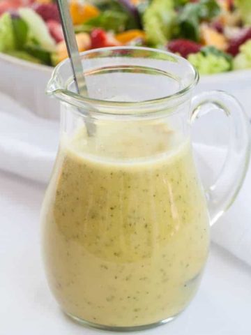 a small pitcher of Everyday Honey Citrus Vinaigrette with salad in the background