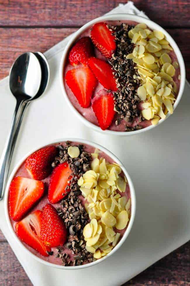 Strawberry Chia Smoothie Bowl. Two bowls garnished with strawberries, almonds and cacao nibs.