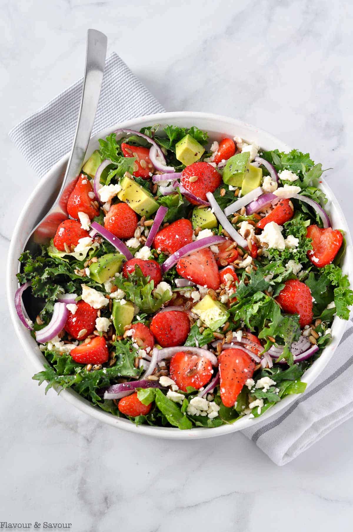 Overhead view of Strawberry Kale Salad with Poppy Seed Dressing on a marble slab.