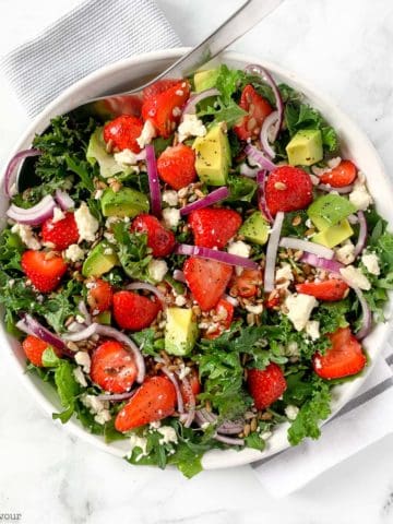 overhead view of a round white dish of Strawberry Kale Salad