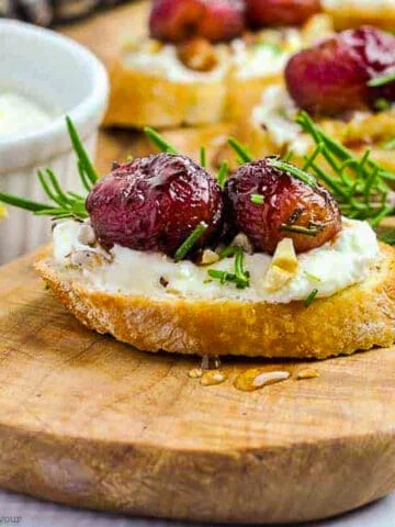 close up view of a crostini appetizer with roasted grapes and whipped goat cheese