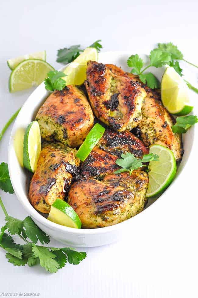 Easy Thai Baked Chicken thighs in an oval serving dish with lime wedges and cilantro leaves.