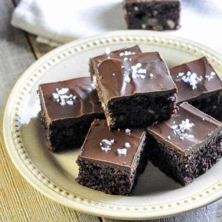 Brownies topped with frosting and flaky salt on a round plate