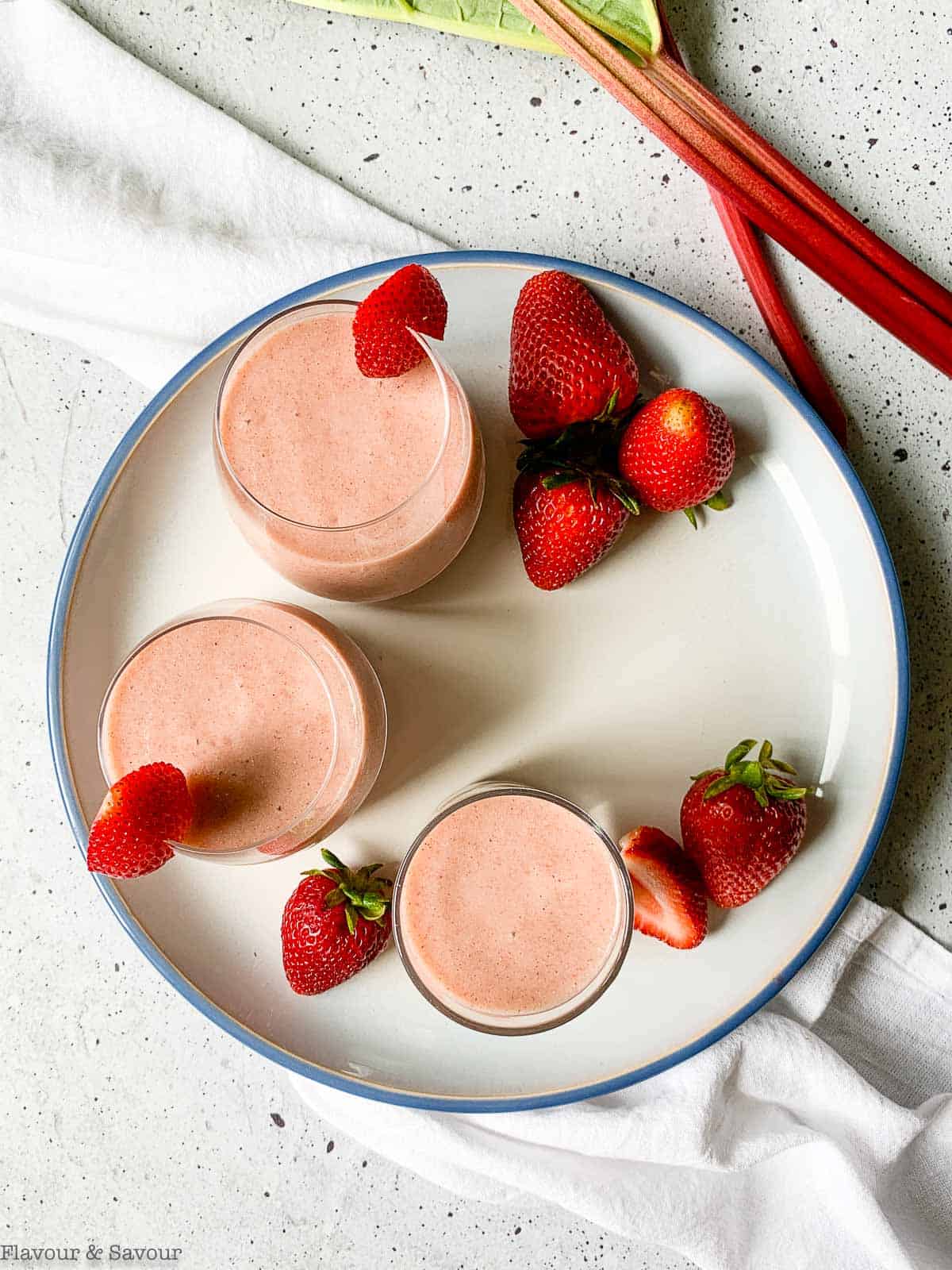 Overhead view of 3 glasses of strawberry rhubarb smoothie with fresh berries