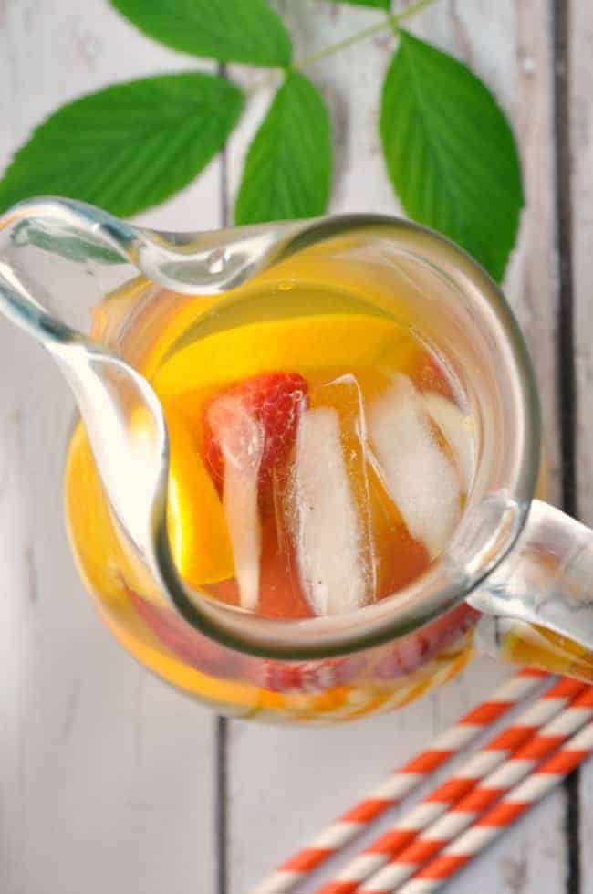 Overhead view of a pitcher of Raspberry Leaf, Rosemary and Orange Iced Tea with a fresh raspberry leaf