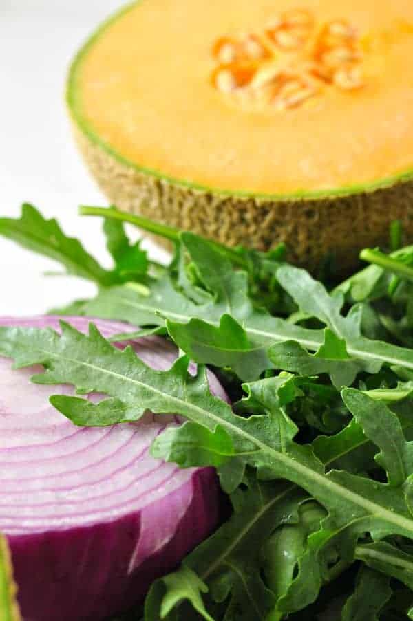 Half a cantaloupe, arugula leaves and a cut red onion.