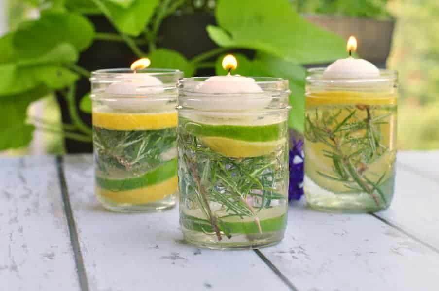 Natural Bug Repellent Luminaries using essential oils in small Mason jars with herbs and lemon and lime slices.