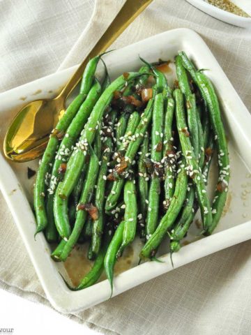 Sesame Ginger Green Beans in a square serving dish with a gold spoon
