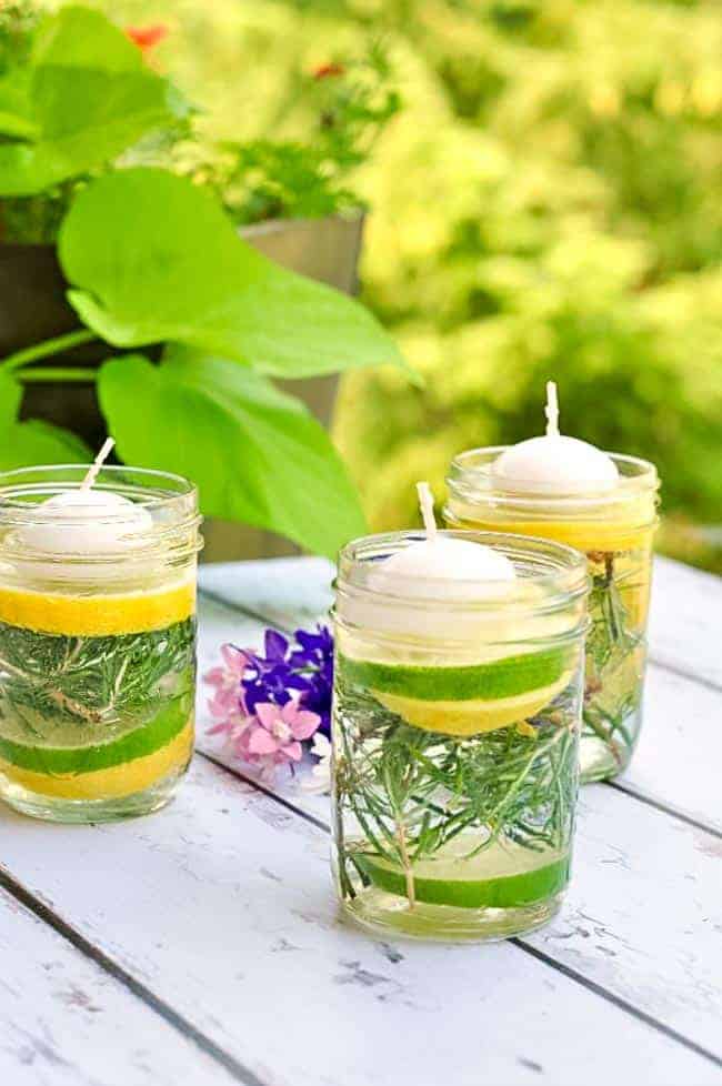 Natural bug Repellent Luminaries using essential oils in Mason jars with lemon and lime slices, herbs, and a floating candle.