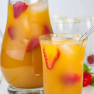 A pitcher and a glass of Peach Ginger Iced Green Tea garnished with strawberries.