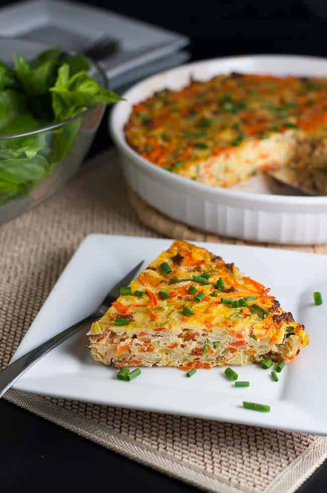 A wedge of kohlrabi quiche on a plate with the quiche dish in the background.