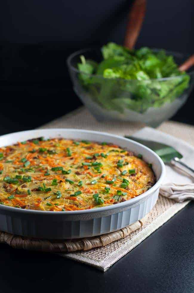 A crustless quiche in a white quiche dish with a bowl of salad in the background.