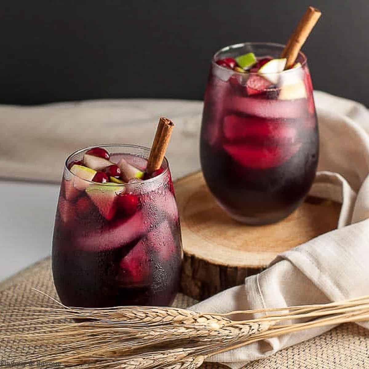 Two glasses of cranberry apple cider sangria with chopped apples and cinnamon sticks.