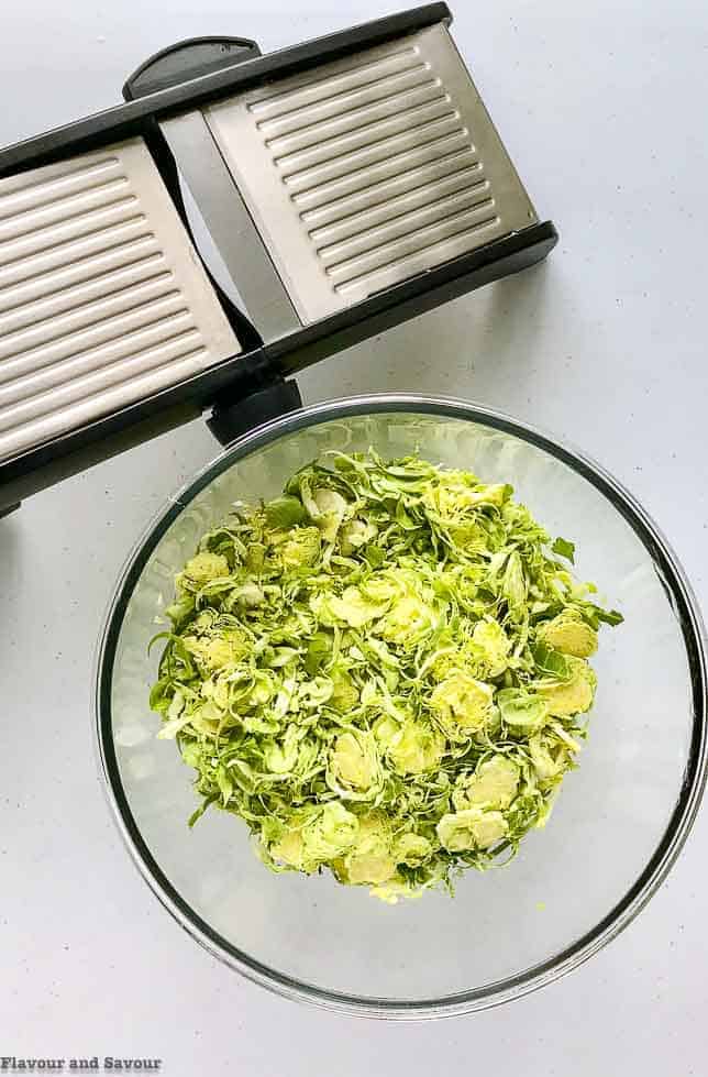 Shredding sprouts for Shaved Brussels Sprouts Salad with Apples, Cranberries and Pecans using a mandolin slicer.