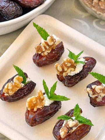 Dates stuffed with goat cheese, walnuts and mint on a square plate.