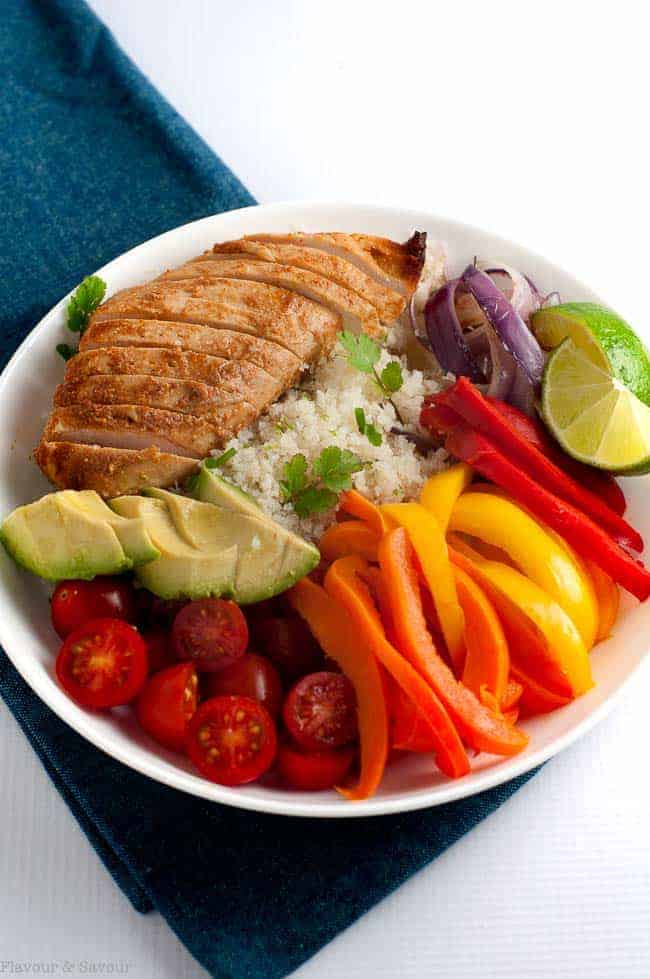 Overhead image of a white bowl with sliced chicken breast, peppers, tomatoes and avocado