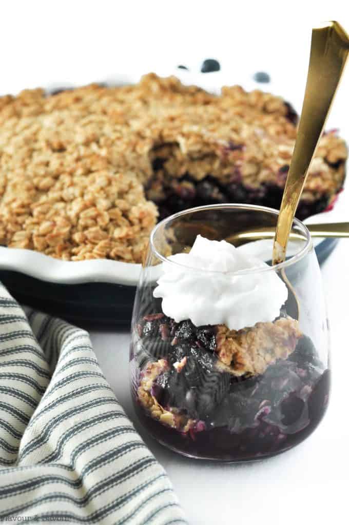 Blueberry Crisp in a dessert glass with a baking dish in the background