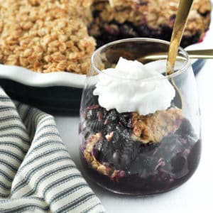 Blueberry Crisp with Limoncello in a dessert glass with whipped cream and a spoon