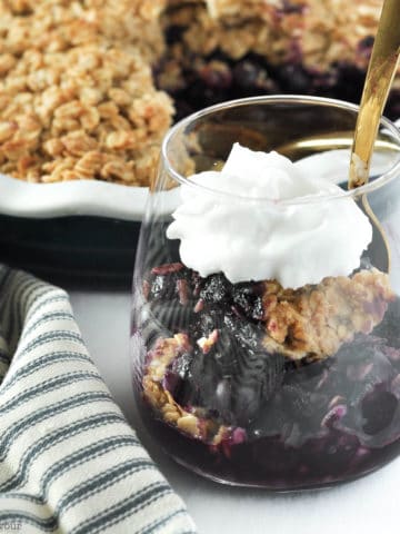 Blueberry Crisp with Limoncello in a dessert glass with whipped cream and a spoon