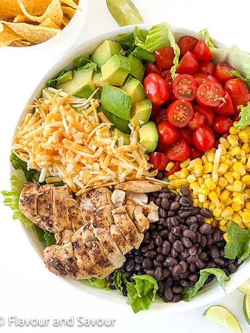 Overhead view of ingredients for chopped chicken taco salad in sections in a shallow white serving bowl.