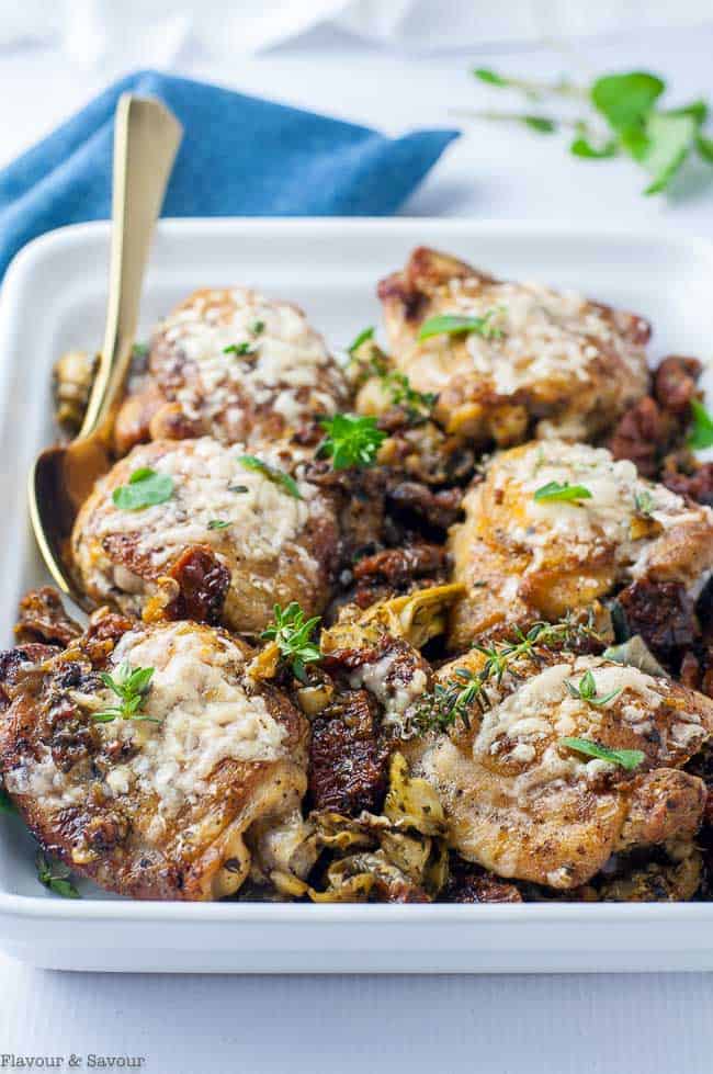 Baked Sun-dried Tomato and Artichoke Chicken thighs in a white baking dish.