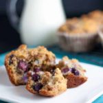 A muffin on a plate with a pitcher of milk in the background