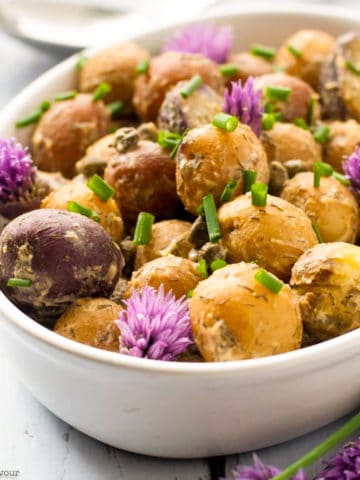 A bowl of potato salad garnished with chives and chive flowers.